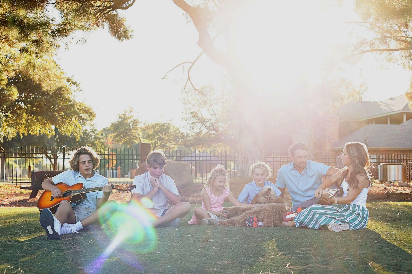 The Gotcher family sitting in the grass singing together, with guitars, in warm evening sunlight
